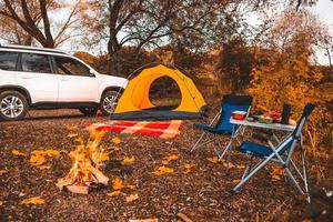 camping herfstplaats met vreugdevuur en draagbare stoelen foto