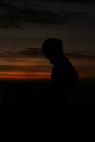 silhouet van een jong Mens staand door de meer genieten van de zonsondergang. vredig atmosfeer in natuur foto