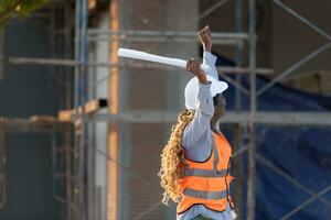 Bij de gebouw plaats, een vrouw ingenieur houdt een blauwdruk in hand- en verhoogt haar handen in vreugde. foto