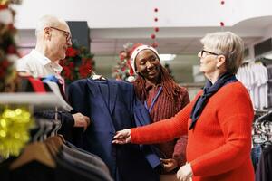 verkoop assistent Holding pak jasje voor senior mensen, aanbevelen perfect kleren voor Kerstmis vooravond kleding. vrouw op te slaan werknemer helpen klanten kopen formeel kleding, presenteren handelswaar. foto