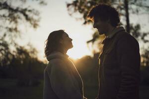 portret van gelukkig liefhebbend paar in park in zonsondergang. paar in silhouet op zoek Bij elk ander. foto