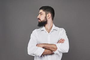 jonge knappe man met een baard leunend tegen grijze muur met gekruiste armen. foto