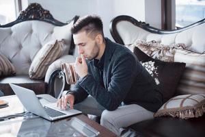 jonge zakenman die aan modern loftkantoor werkt. man met wit overhemd en met behulp van hedendaagse laptop. panoramische vensters achtergrond