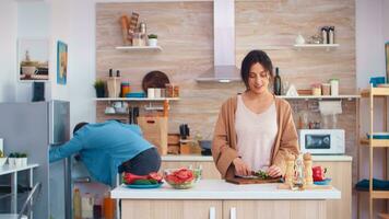 vrouw snijden komkommers Aan houten snijdend bord voor gezond salade. man opening koelkast. Koken voorbereidingen treffen gezond biologisch voedsel gelukkig samen levensstijl. vrolijk maaltijd in familie met groenten foto