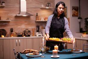 gelukkig vrouw voorbereidingen treffen romantisch avondeten en Holding bord met druiven en kaas in dining kamer. jong Kaukasisch dame Koken voor haar man een romantisch diner, aan het wachten in keuken. foto