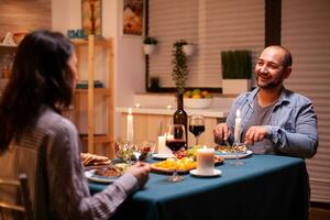 geliefden genieten van smakelijk voedsel terwijl hebben avondeten in keuken. kom tot rust gelukkig mensen, zittend Bij tafel in keuken, genieten van de maaltijd, vieren verjaardag in de dining kamer. foto