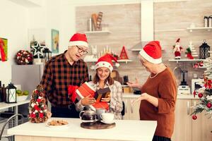 vrolijk kleinkind genieten van Kerstmis ontvangen presenteert van senior Mens en vrouw vervelend de kerstman hoed. gelukkig liefhebbend grootouders vieren winter vakantie en verhouding met kleindochter in huis met Kerstmis decoratie. foto