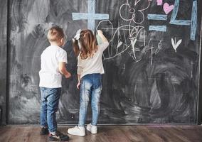 schattig klein meisje en jongen tekenen met kleurpotlood op de muur. werken van kind. leuke leerling die op bord schrijft foto