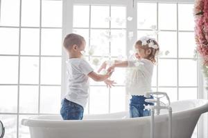 kind spelen met rozenblaadjes in huis badkamer. klein meisje en jongen samen plezier en vreugde. het concept van de kindertijd en de realisatie van dromen, fantasie, verbeelding foto