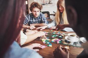 groep creatieve vrienden zitten aan houten tafel. mensen die plezier hebben tijdens het spelen van een bordspel foto