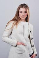lachende blonde vrouw in stijlvol vest poseren in wollen trui poseren tegen een witte muur