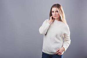 portret van mooie jonge vrouw in witte trui en jeans, geïsoleerd op een grijze achtergrond foto