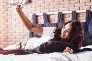 gelukkig mooi Afrikaans meisje in nachtkleding die zich uitstrekt glimlachend zittend op bed thuis werd 's ochtends wakker op een zonnige dag foto