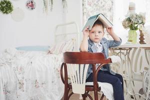 foto van ijverige schooljongen met boek op zijn hoofd huiswerk maken. de schooljongen is het huiswerk beu