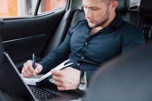 een jonge zakenman regelt zijn zaken met een notitieblok terwijl hij achter in de auto zit foto