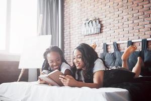 twee mooie Afrikaanse meisje in nachtkleding glimlachend zittend op bed thuis wakker in de ochtend op een zonnige dag.