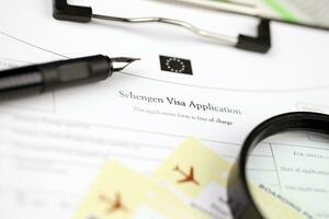 schengen Visa toepassing Aan a4 tablet leugens Aan kantoor tafel met pen en vergroten glas foto