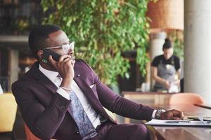 portret van een jonge en knappe Afro-Amerikaanse zakenman die in een pak aan de telefoon praat. voorbereiding van een zakelijke bijeenkomst. foto
