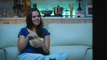 vrouw genieten van de avond aan het kijken TV serie Bij huis zittend Aan comfortabel bankstel gekleed in pyjama. opgewonden geamuseerd huis alleen dame aan het eten snacks en drinken sap Aan knus sofa in leven kamer. foto