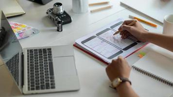 ontwerper schetst een smartphonescherm voor toekomstige klanten op het bureau met laptop en briefpapier. foto