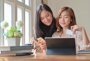 twee tienermeisjes winkelen online met een tablet thuis om online met creditcard te bestellen en te betalen. foto