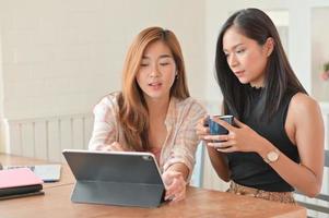 twee aziatische vrouwen die een koffiekopje vasthouden en een laptop gebruiken, bespreken plannen voor haar volgende project. foto