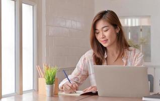 vrouwelijke tienerstudent maakt aantekeningen en studeert thuis online met een laptop.