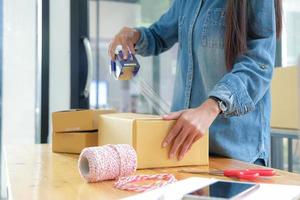 tienermeisjes verpakken producten in dozen en gebruiken doorzichtig plakband om aan klanten te leveren. foto
