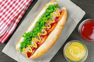 eigengemaakt heet hond met mosterd, ketchup, tomaat en vers salade bladeren Aan zwart leisteen achtergrond foto