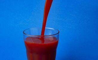 tomaat sap gieten in glas, geïsoleerd Aan blauw achtergrond, met kopiëren ruimte foto