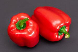 twee vers rood zoet klok paprika's Aan zwart achtergrond foto