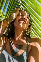 glimlachen vrouw nemen selfie onder palm blad Aan tropisch strand. zomers vakanties moment. foto