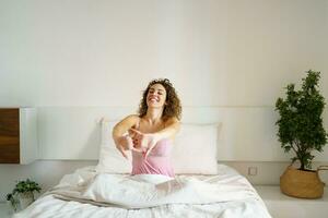 vrolijk vrouw zittend Aan bed in nachtkleding foto