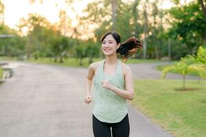 fit Aziatisch jong vrouw jogging in park glimlachen gelukkig rennen en genieten van een gezond buitenshuis levensstijl. vrouw jogger. geschiktheid loper meisje in openbaar park. gezond levensstijl en welzijn wezen concept foto