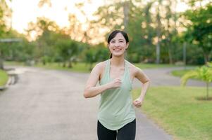 fit Aziatisch jong vrouw jogging in park glimlachen gelukkig rennen en genieten van een gezond buitenshuis levensstijl. vrouw jogger. geschiktheid loper meisje in openbaar park. gezond levensstijl en welzijn wezen concept foto