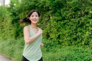 fit Aziatisch jong vrouw jogging in park glimlachen gelukkig rennen en genieten van een gezond buitenshuis levensstijl. vrouw jogger. geschiktheid loper meisje in openbaar park. gezond levensstijl en welzijn wezen concept foto