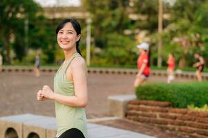 vrouw jogger. fit jong Aziatisch vrouw met groen sportkleding aerobics dans oefening in park en genieten van een gezond buitenshuis. geschiktheid loper meisje in openbaar park. welzijn wezen concept foto