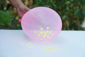 detailopname hand- houden roze ballon naar Doen wetenschap experiment over statisch elektriciteit van ballon en stukken van papier. concept, wetenschap les, pret en gemakkelijk experiment. onderwijs. onderwijs AIDS. foto