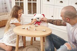 aanbiddelijk dochter vervelend een wit jurk waarmee haar liefhebbend vader. ze zijn drinken thee van een speelgoed- gerechten in een modern kinderen kamer. gelukkig familie. foto