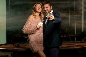 vrouw en Mens poker spelers staand in casino Holding paar- van azen en glas van whisky foto