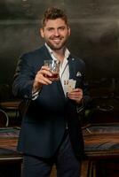 glimlachen vent met twee azen in hand- verhogen glas van whisky naar geslaagd poker spel foto