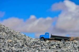 een blauw speelgoed- vrachtauto is zittend Aan top van een stapel van grind foto