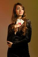 brunette vrouw in zwart jurk tonen twee rood chips en azen, poseren tegen kleurrijk studio achtergrond. gokken, poker, casino. detailopname. foto