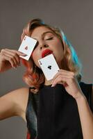 blond meisje in zwart elegant jurk tonen twee spelen kaarten, poseren tegen grijs achtergrond. het gokken amusement, poker, casino. detailopname. foto