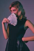 blond meisje in zwart elegant jurk Holding sommige geld, poseren tegen kleurrijk achtergrond. het gokken amusement, poker, casino. detailopname. foto