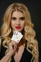 blond meisje in zwart jurk en ketting. ze is lachend, tonen twee spelen kaarten, poseren Aan zwart achtergrond. poker, casino. detailopname foto