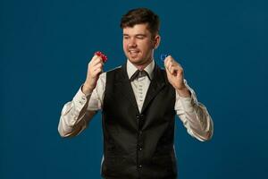 nieuweling in poker, in zwart hesje en wit shirt. Holding sommige gekleurde chips. poseren tegen blauw achtergrond. gokken, casino. detailopname. foto