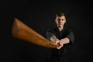 kendo goeroe vervelend in een traditioneel Japans kimono is beoefenen krijgshaftig kunst met de shinai bamboe zwaard tegen een zwart studio achtergrond. foto