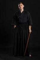 kendo goeroe vervelend in een traditioneel Japans kimono is beoefenen krijgshaftig kunst met de shinai bamboe zwaard tegen een zwart studio achtergrond. foto