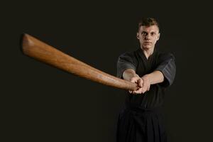 kendo goeroe vervelend in een traditioneel Japans kimono is beoefenen krijgshaftig kunst met de shinai bamboe zwaard tegen een zwart studio achtergrond. foto